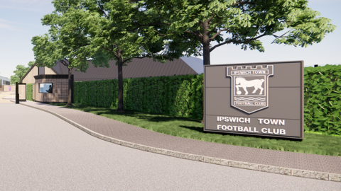 A CGI image of how the new entrance to Playford Road could look. There is a road leading to gates, with a bush and trees running alongside the road. At the end of the road furthest from the entrance is a grey sign that reads "Ipswich Town Football Club", with the club crest on. The crest has a Suffolk Punch horse with its hoof on a football.