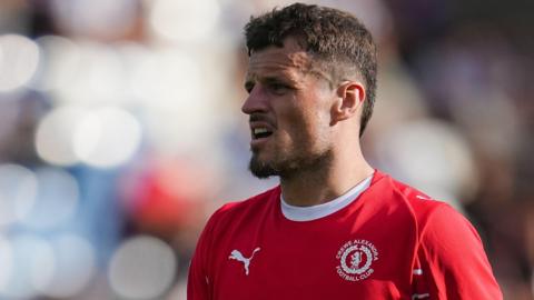 Crewe striker Josh March looks to his right during a match. He is wearing a red Crewe home shirt.