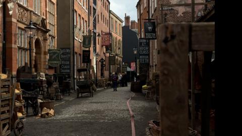 A cobbled street is dressed as Victorian London, with period signs, props, and buildings.
