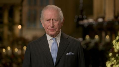 King Charles wearing a black suit and blue tie.