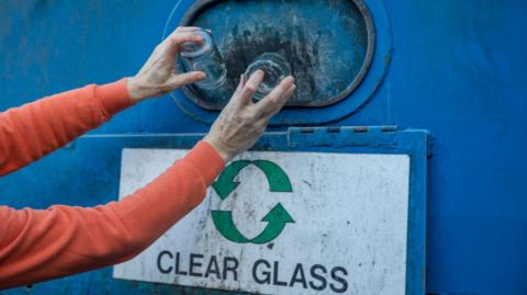 Woman hand dropping off her home glass recycling at a recycling hub