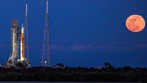 Artemis II rocket on the launch pad in Cape Canaveral with a full, bright and orange Moon rising in the sky next to it
