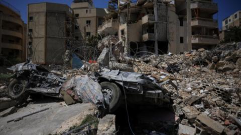 A damaged building, rubble and a destroyed vehicle in the aftermath of Israeli strikes