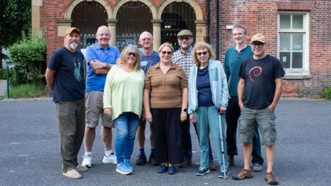 A small group of men and women pose together in front of a fine looking red brick building 