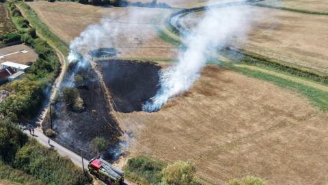 The image shows part of a field that has burned from a fire; a fire engine can be seen beside the field.