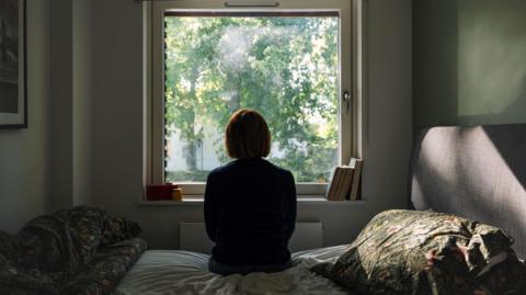 Silhouette of a woman sitting on a bed looking out a window