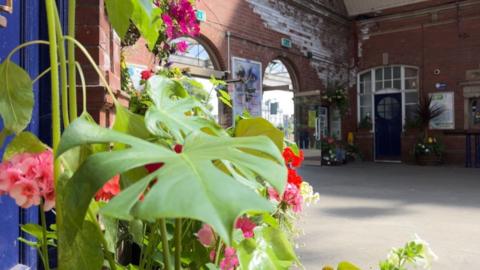 Pink flowers and green leaves in the foreground with the red-brick walls of Bridlington station in the background