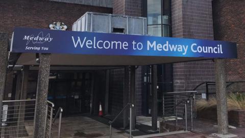 The entrance to a brown-bricked building. There is a blue sign which says "Welcome to Medway".