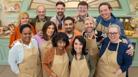 GBBO cast standing in kitchen smiling