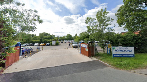 The entrance to Johnsons Coaches with a yellow and black barrier and wooden fencing.