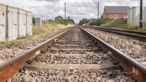 Train tracks stretch off into the distance. The rails go off as far as the eye can see, and small stones and rocks surround the railway sleepers underneath.