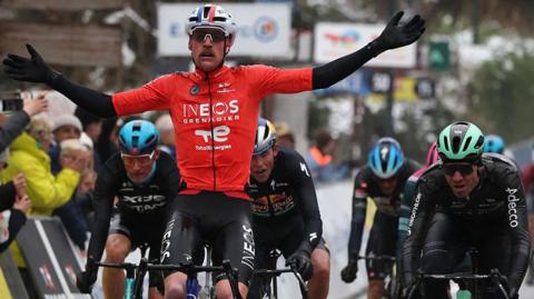 Dorian Godon holds out his arms as he rides his bicycle next to several other competitors