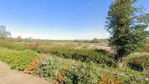 Fields and foliage can be seen as well as wooden fencing.