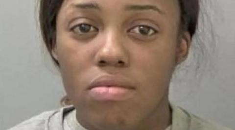A mug shot of a woman with dark hair tied back and wearing a light grey top