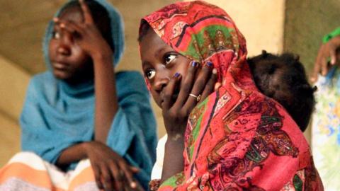 Two young women - one wearing a red headscarf and the other in a blue headscarf, sit at a shelter where they were evacuated by the Sudanese army in Omdurman - May 2025.