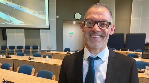 A picture of a council leader Adam Zerny in a black suit with a dark green tie