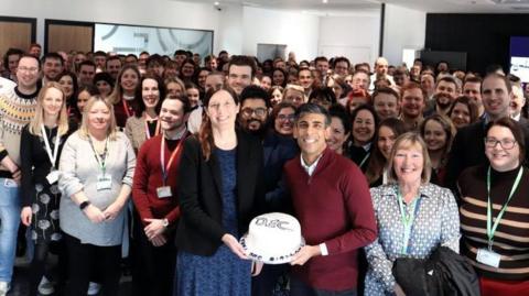 Prime Minister Rishi Sunak holding a cake surrounded by staff from the Darlington Economic Campus