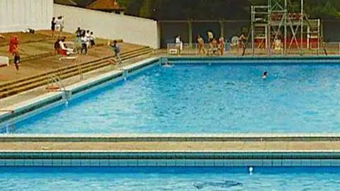 Broomhill lido pictured in 1969. Blue tiles in the shape of a whale can be seen at the bottom of the pool. There are people sitting around the edge of the pool. 