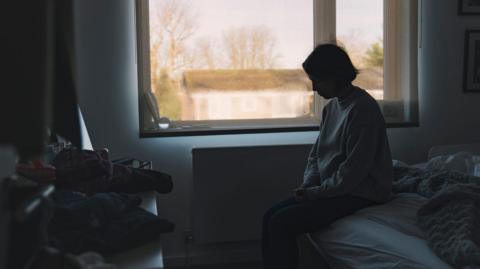 A distressed woman sits on the end of the bed 