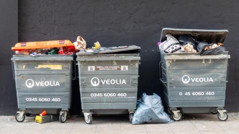 Three large grey industrial waste bins in a row with words Veolia written on each bin