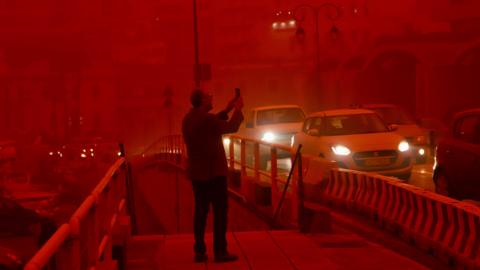 A man takes a picture while cars drive with their headlights on in red air.