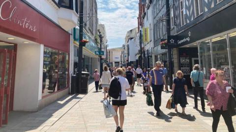 Strand street, with lots of shops and businesses on both sides of the image and people walking along the street.