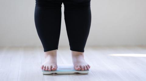 An anonymous woman who is overweight stands on some weighing scales