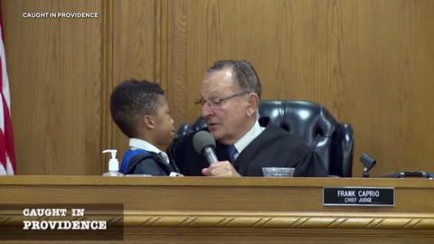 A little boy next to Frank Caprio in court as the judge asks him a question on the microphone