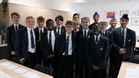 A photo of a group of teenagers standing and smiling into the camera they are all wearing a school uniform. 