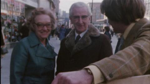 Two people reading a sign held by a reporter on the streets of Bristol.