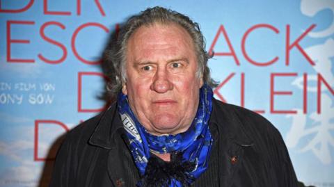 Gérard Depardieu appears at a film premiere wearing a blue scarf in front of a film poster. File photo