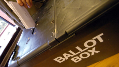 A ballot paper being pushed into the slot of a ballot box