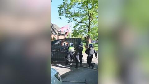 Three police officers push a gate