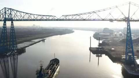 Middlesbrough's Transporter Bridge on an overcast day - there is a boat going under the bridge. Hazy light is reflected in the water.
