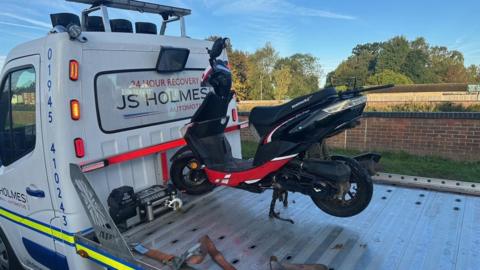 A black and red moped loaded on a white lorry.