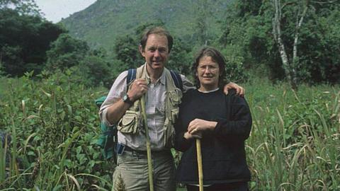 Bleddyn and Sue Wynn Jones in tall grass with trees and mountains in the background
