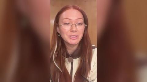 Elz The Witch has long red hair and is wearing rimless glasses and a cream jacket.