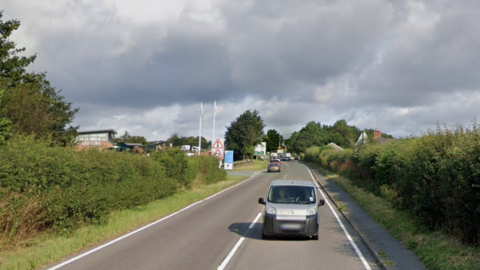 A leisure centre building is on the left hand side of a stretch of road. There is a silver car in the frame.