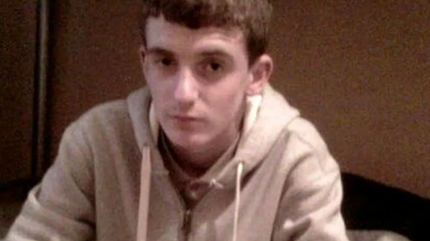 Kevin Wilson, who has brown hair and is wearing a grey zip-up hoody, looks into the camera with a serious expression. 