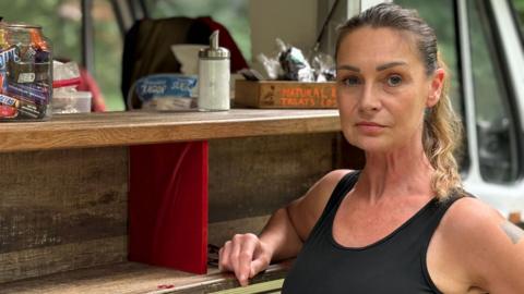 A woman in a black vest top stands in front of a food truck