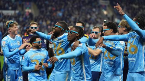 Sky Blues players, including Victor Torp, Jay Dasilva, Frank Onyeke, Brandon Thomas-Asante, Joel Latibeaudiare and Haji Wright celebrate winning the EFL Championship title. They are wearing the club's home kit, with some wearing shirts celebrating the occasion.