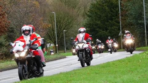 Motorbikes on a main road, driven by people dressed in red Father Christmas suits. 