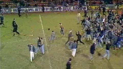 Football fans charge the pitch.