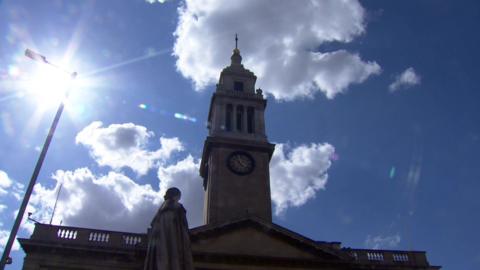 A silhouetted image of Hull's Guildhall, with a blue sky behind it, showing the time ball on top of the building.