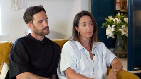 Craig Bowe and his wife Carly sit on their sofa at home as they speak to the BBC