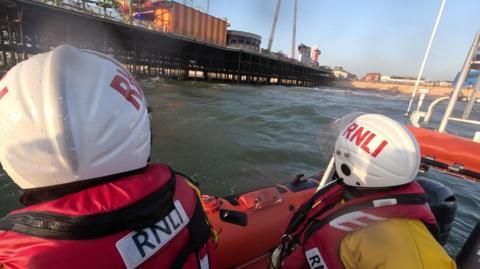 Shot from behind of lifeboat crew in white helmet and red life jackets heading towards Blackpool South pier