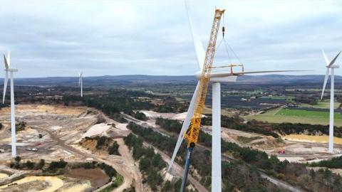 Four white wind turbines set within series of tree-lined pits 