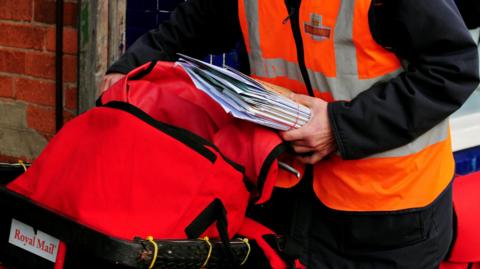 A cropped image of a Royal Mail worker holding a bunch of letters for delivery