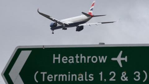 A British Airways passenger plane flies over a road direction sign as it makes its landing approach to Heathrow Airport in west London