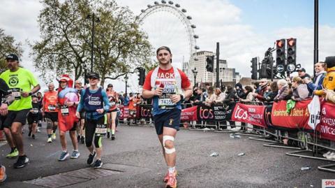 Jack Brown running at the London Marathon in 2024 with runners to the left, spectators to the right and the London Eye behind him.